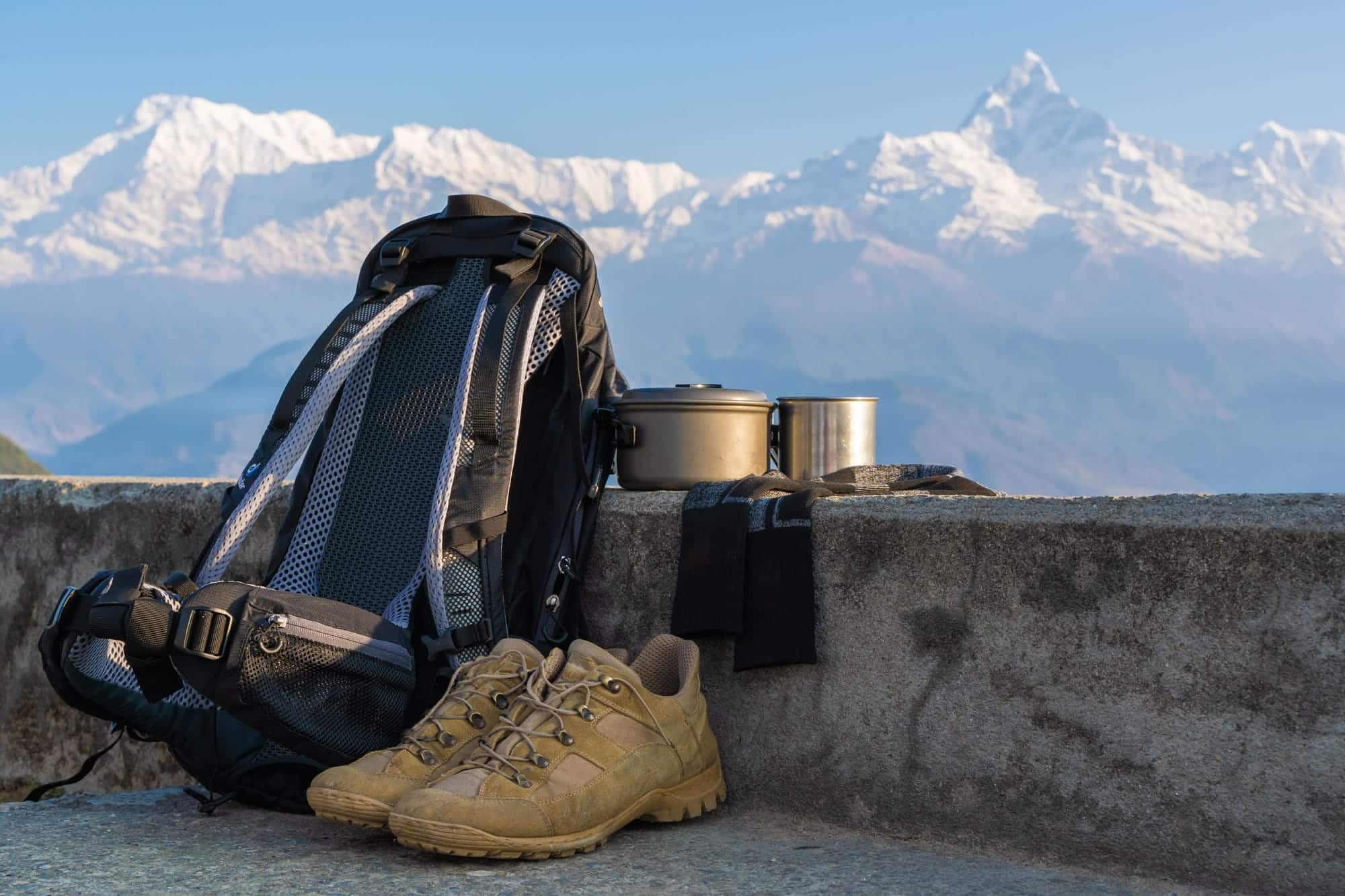 Is Annapurna Base Camp Trek Suitable for Beginners? 2 trecking hiking equipment set with annapurna mountain range background bagpack hiking shoes socks metal cup kettle pot outdoor activity concept